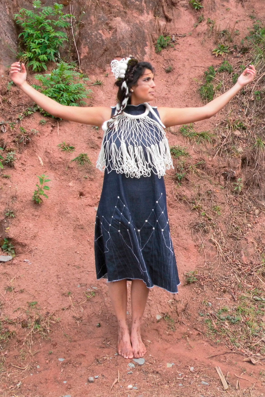Mujer parada al aire libre, manos levantadas con vestido con adorno textil.