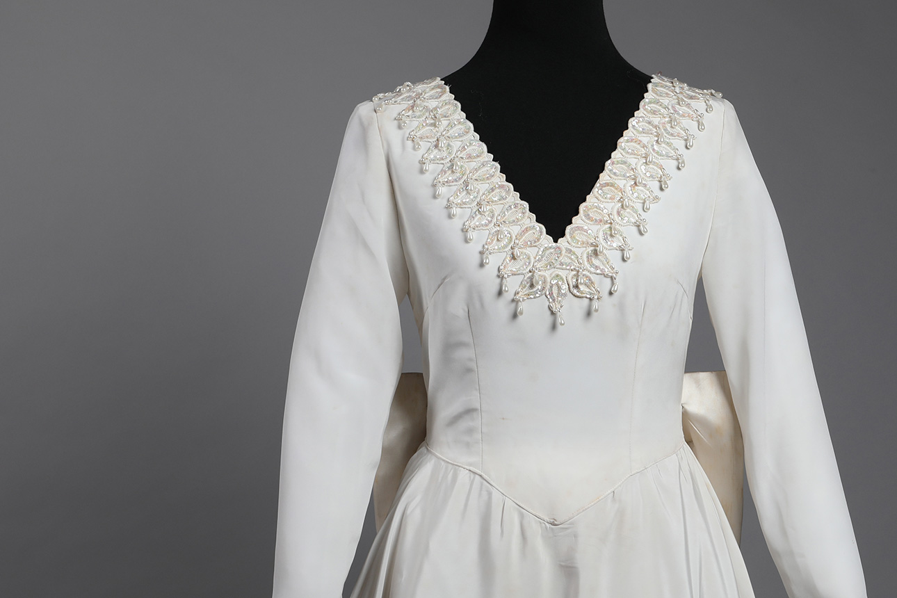 Puede observarse un maniquí negro vistiendo un vestido de novia escote en v de color blanco, de tafeta, con contura ajustada.